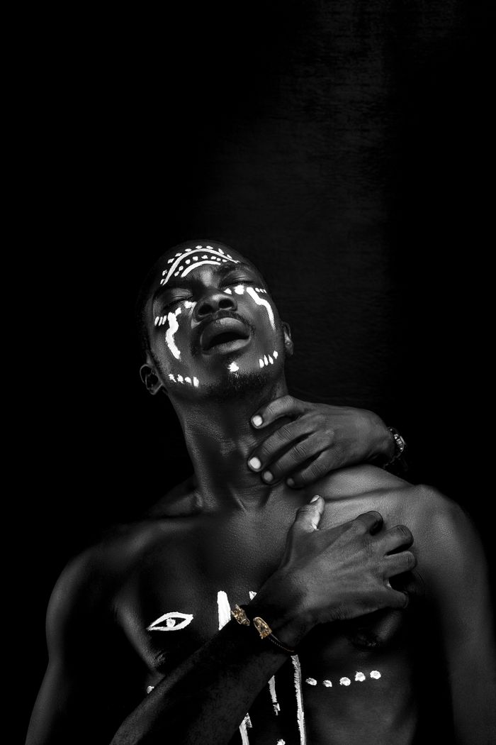Home Black and white artistic portrait of a man in face paint with hands posed dramatically.