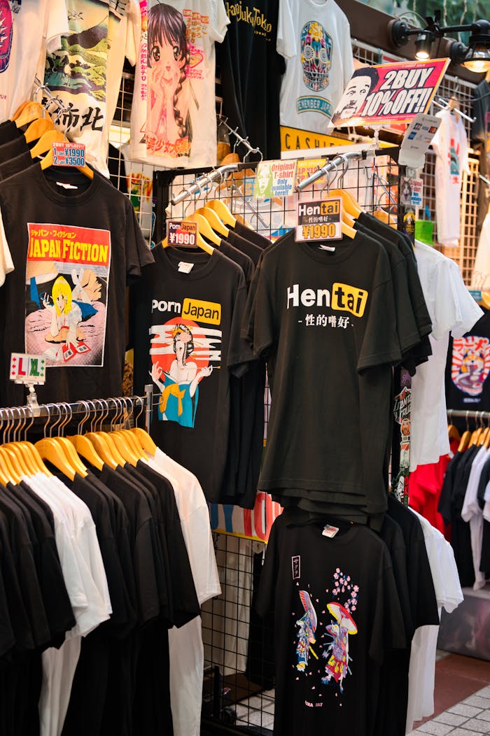 Colorful collection of graphic t-shirts displayed at a bustling Tokyo market stall.