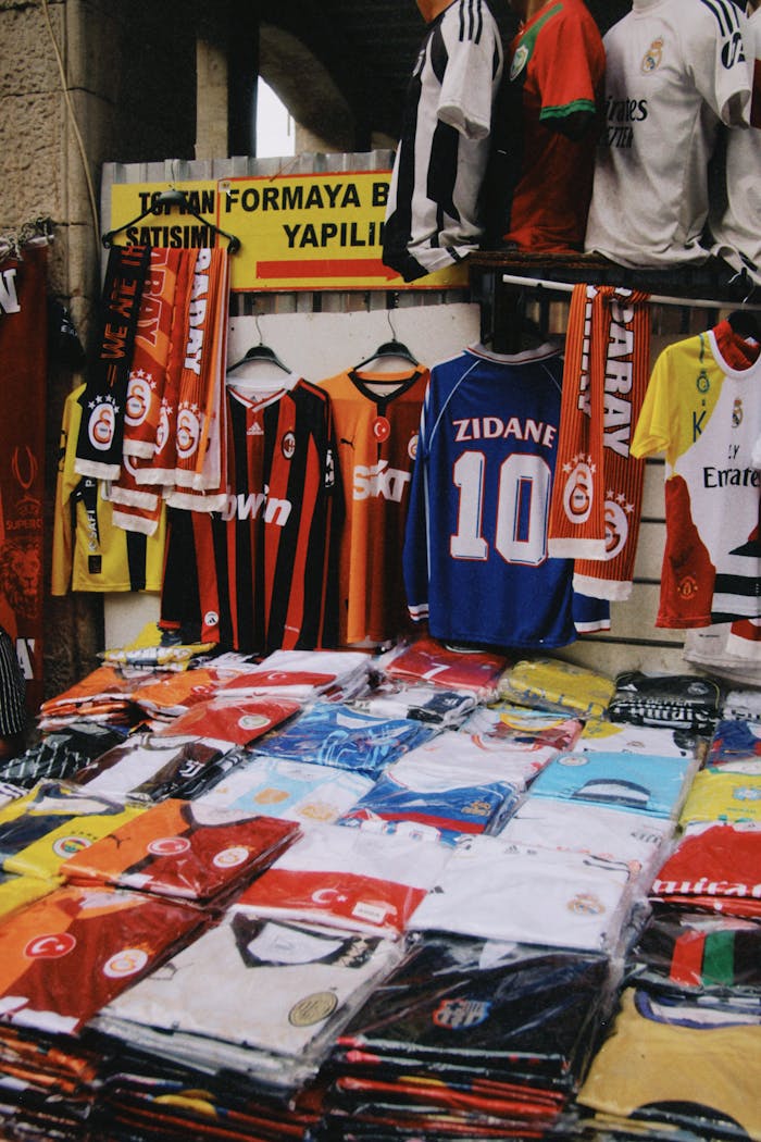A vibrant display of various branded soccer jerseys at an outdoor market stall.