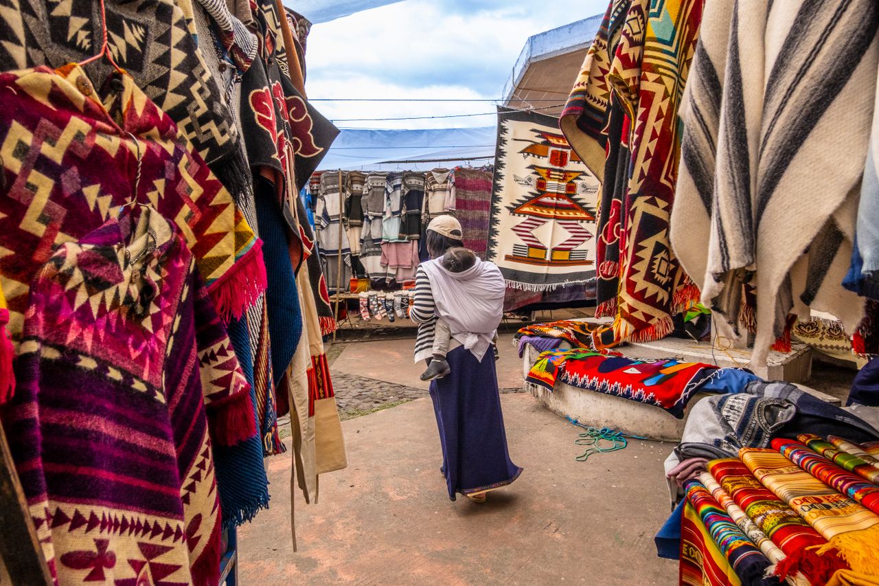 Colorful display of traditional textiles at a bustling outdoor market with a local shopper.
