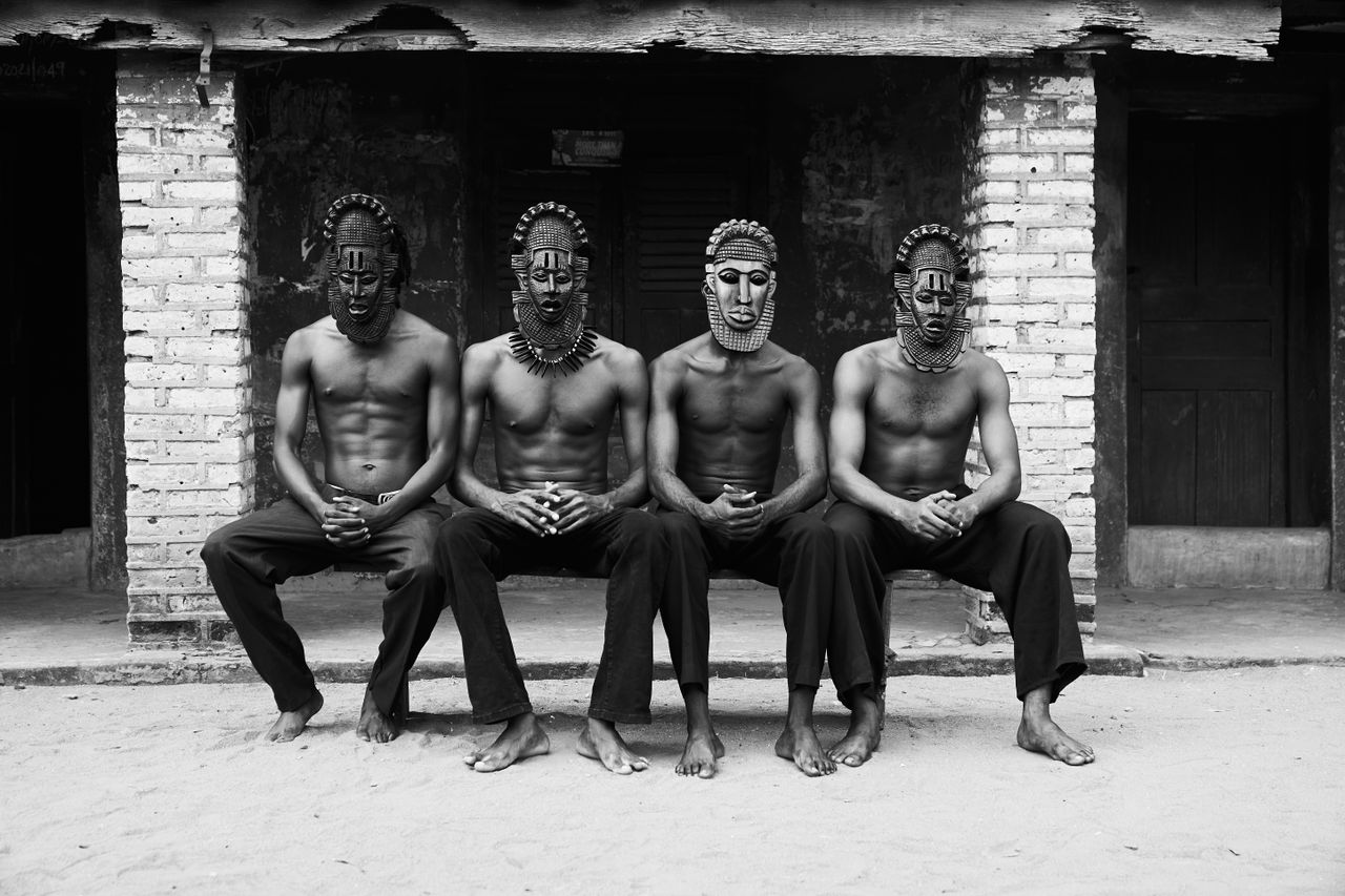 services-01 Four men with traditional masks sit in unity, showcasing cultural heritage.