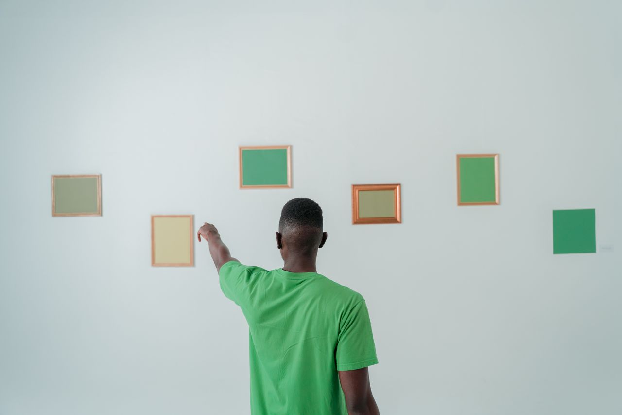 Home Man in a green shirt pointing at framed art pieces on a minimalist wall.